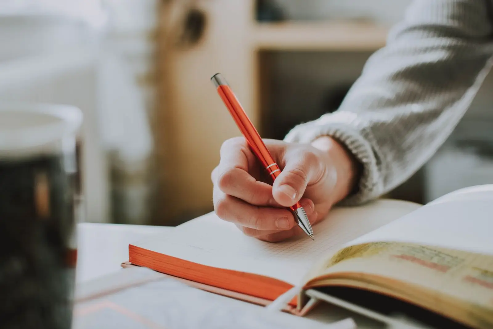 Mano escribiendo en un cuaderno junto a un libro abierto y subrayado